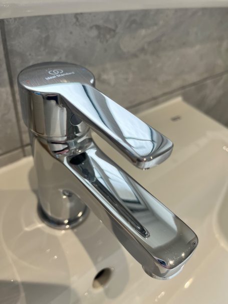 Chrome bathroom tap with two levers mounted on a white sink.
