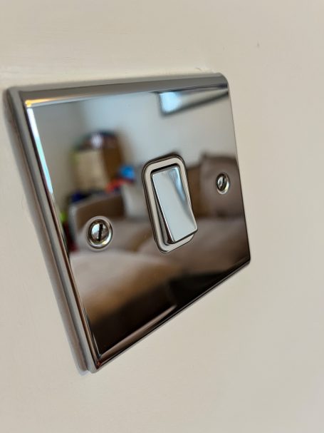 Shiny light switch on a wall, reflecting a blurred interior background.