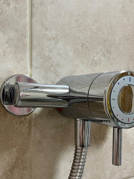 Shiny chrome shower faucet with temperature control dial against tiled wall.